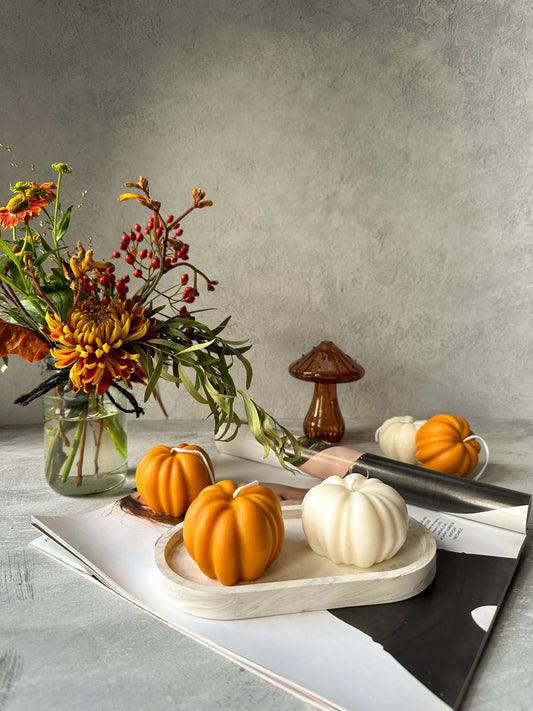 Orange and Ivory Soy Wax Pumpkin Candles on a trinket tray and mushroom glass vase and flowers on the background.