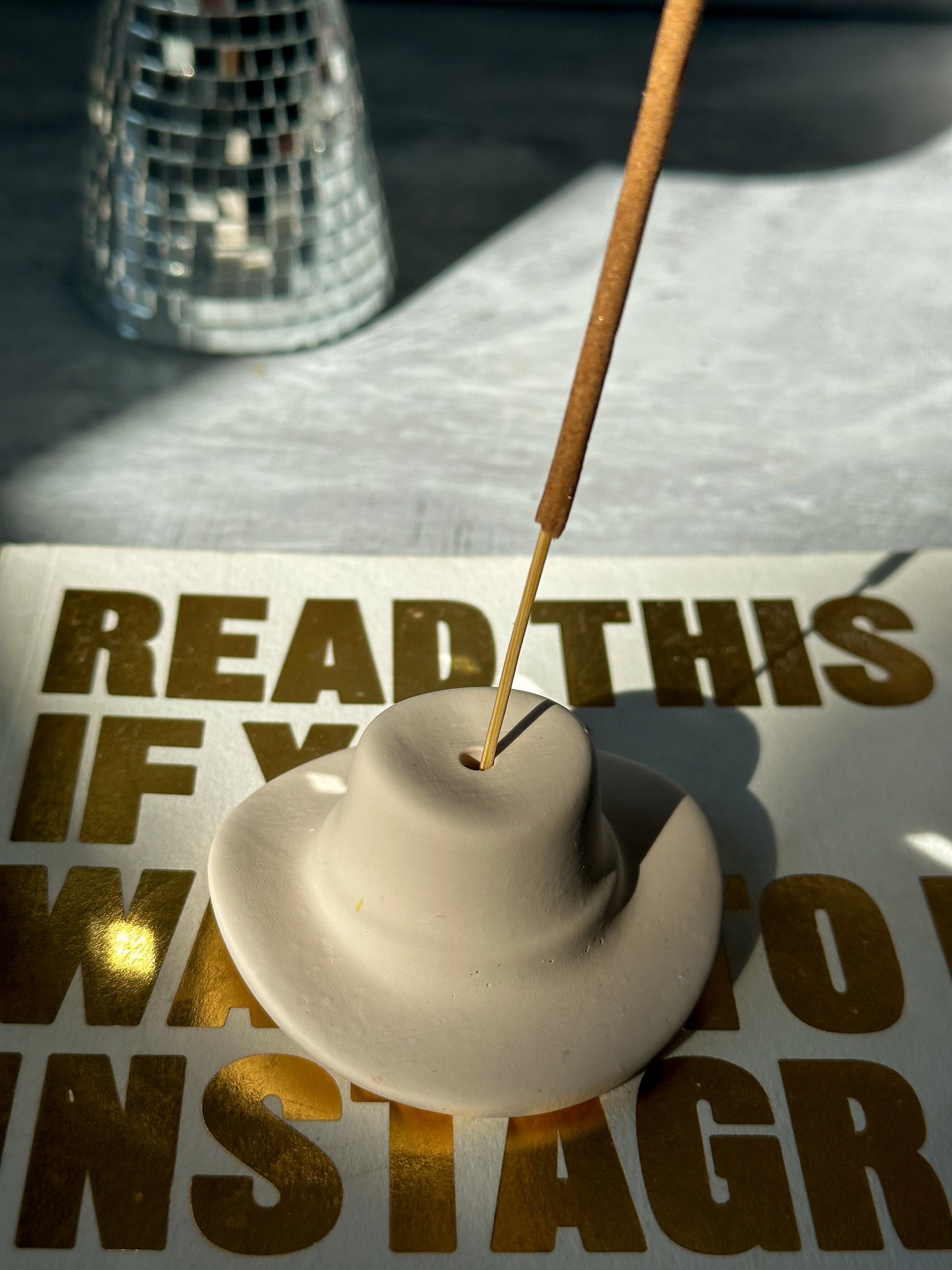 Latte Cowboy Hat Incense Holder with incense in it sitting on a book.