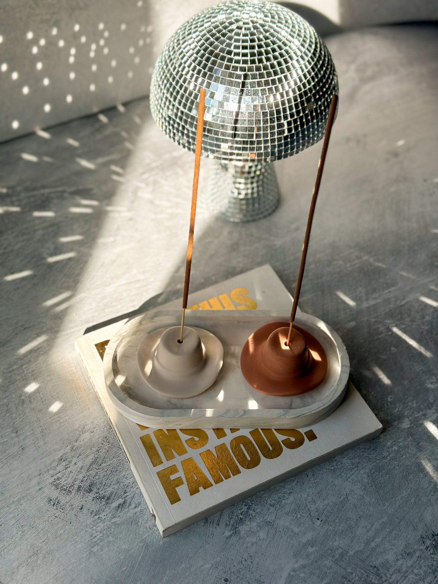 Latte and Terracotta Cowboy Hat Incense Holders with incense in it sitting on a book with mushroom disco ball on the background.