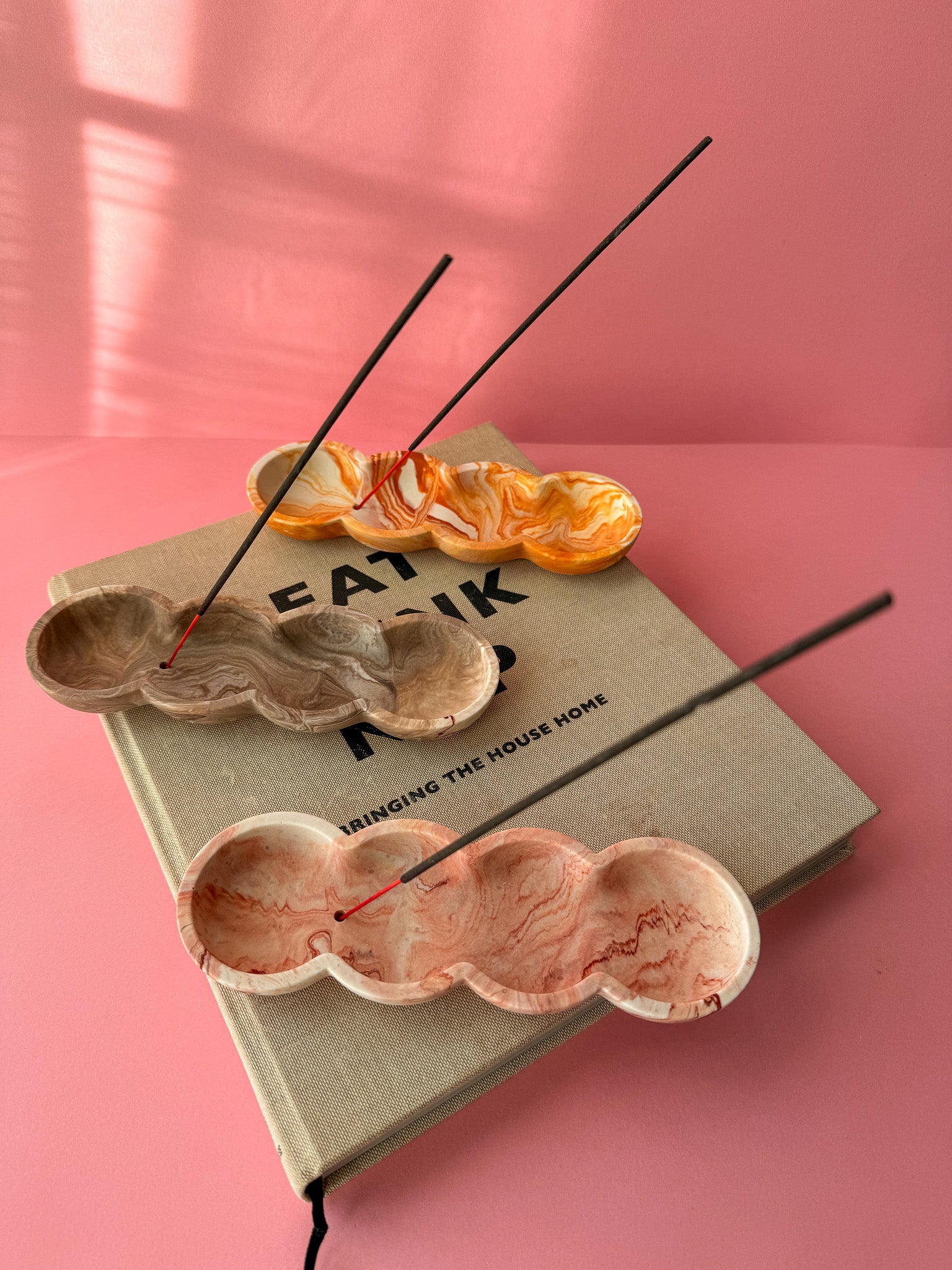 Incense sticks on a decorative book with marbled design against a pink background