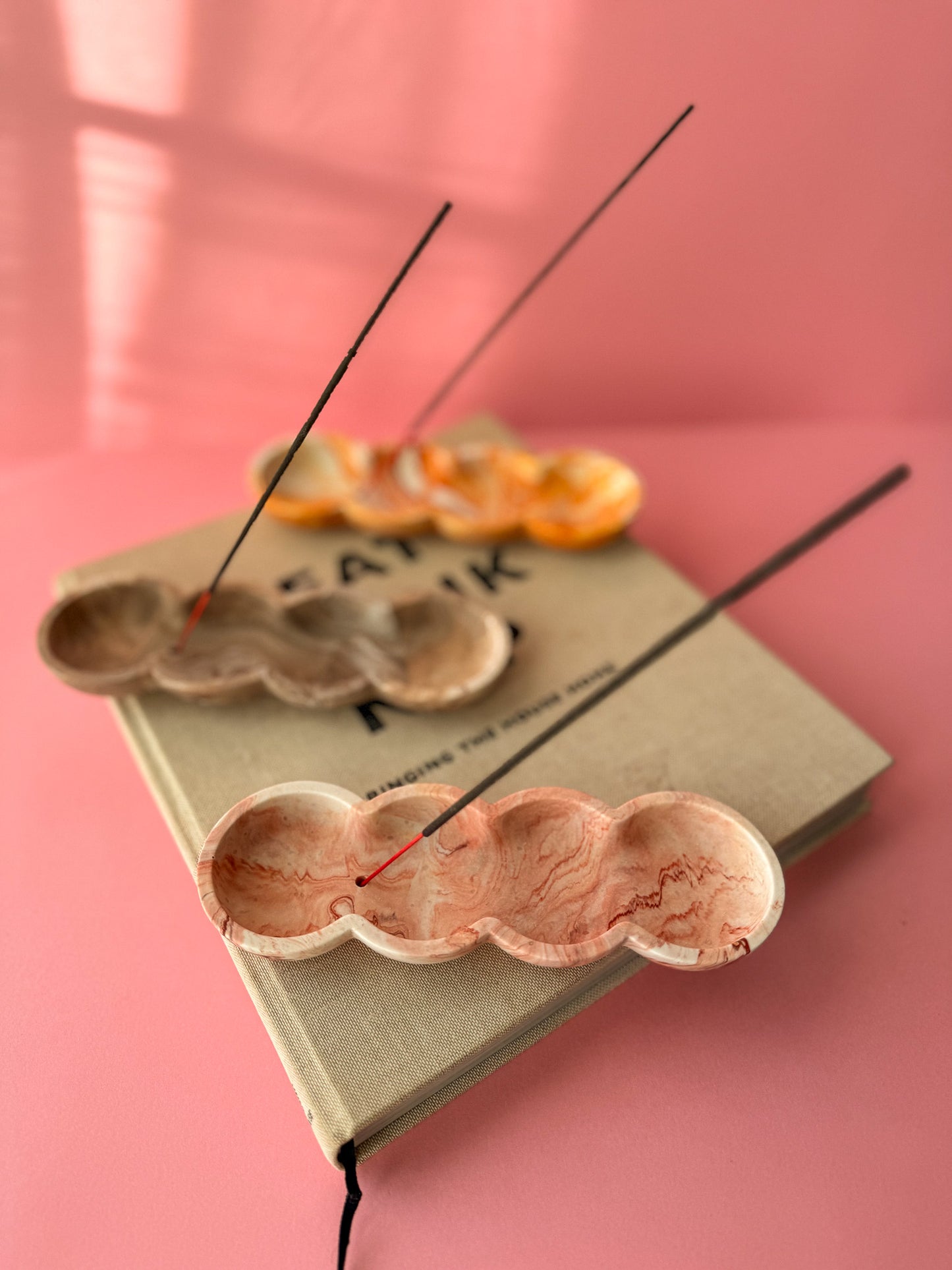 Incense stick holders on a wooden tray with a pink background