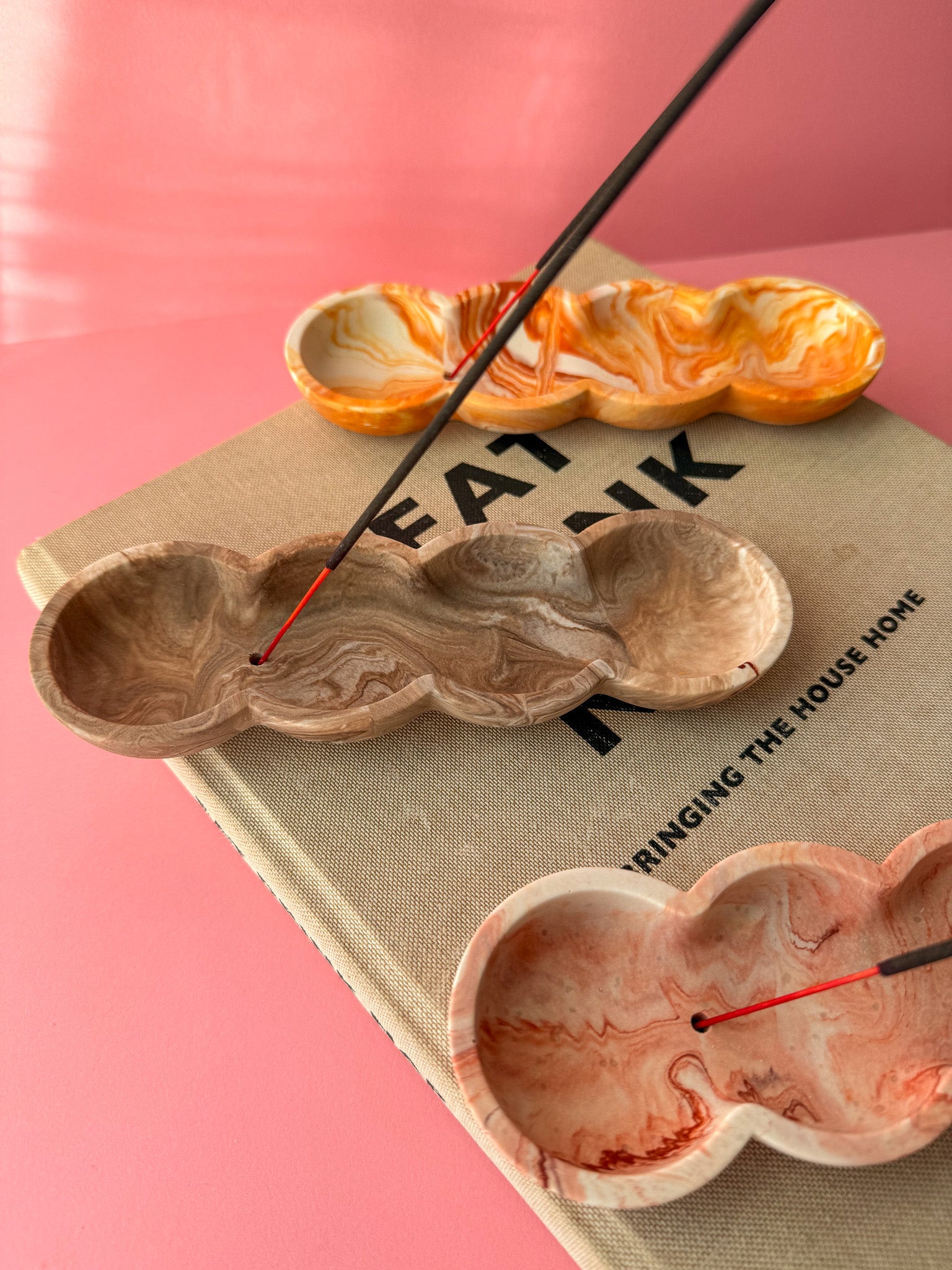 Stoneware incense holder with incense sticks on a book against a pink background