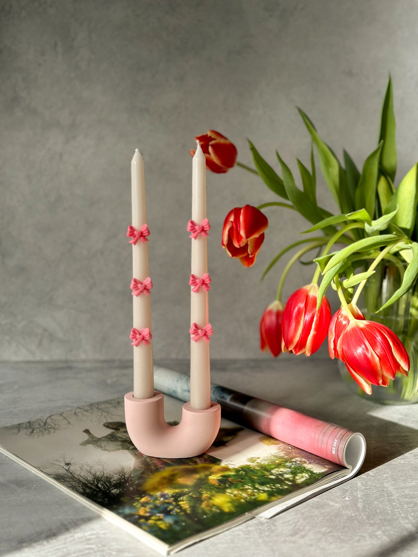 White candle with 3D bow candle with the pink U shape candle holder is on the magazine Tulips on the background