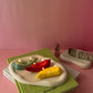 Burning Chile Pepper Candles are red green and yellow sitting on the plate with pink background