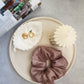 Large Round Decorative Tray on a magazine on the tray there is a scrunchies, pillar candle and leaf shape trinket dish