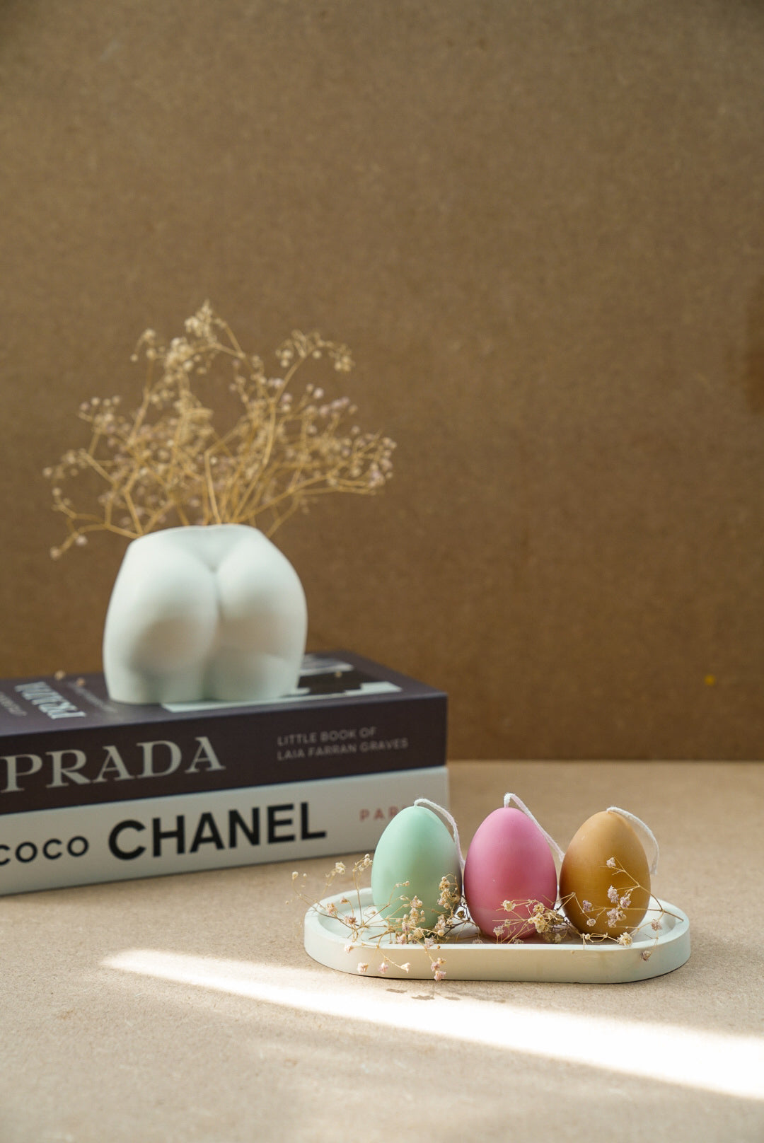 Easter Egg Candles on a trinket tray with dry flowers around and magazine on the background with bum vase on it. 