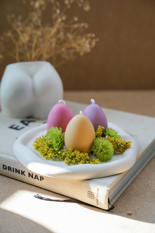 Easter Egg Candles on a trinket dish with green flowers around. 