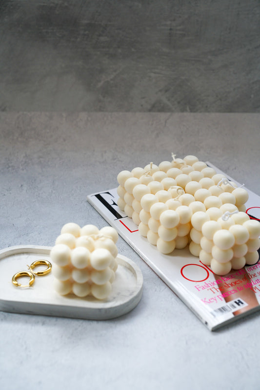 Ivory bubble candle with jewellery tray on a magazine with grey background