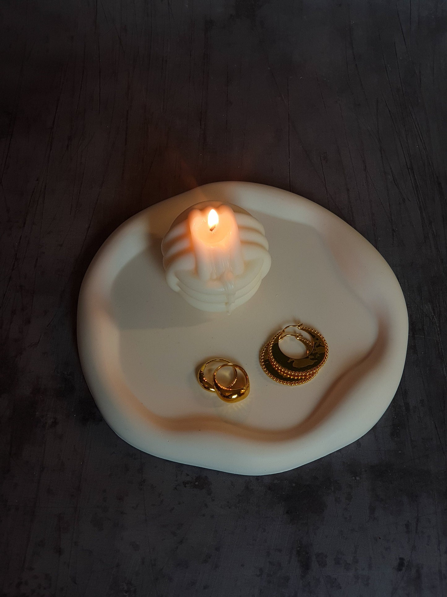 Curvy Round Trinket Tray with candle and jewellery on it with a grey background. 