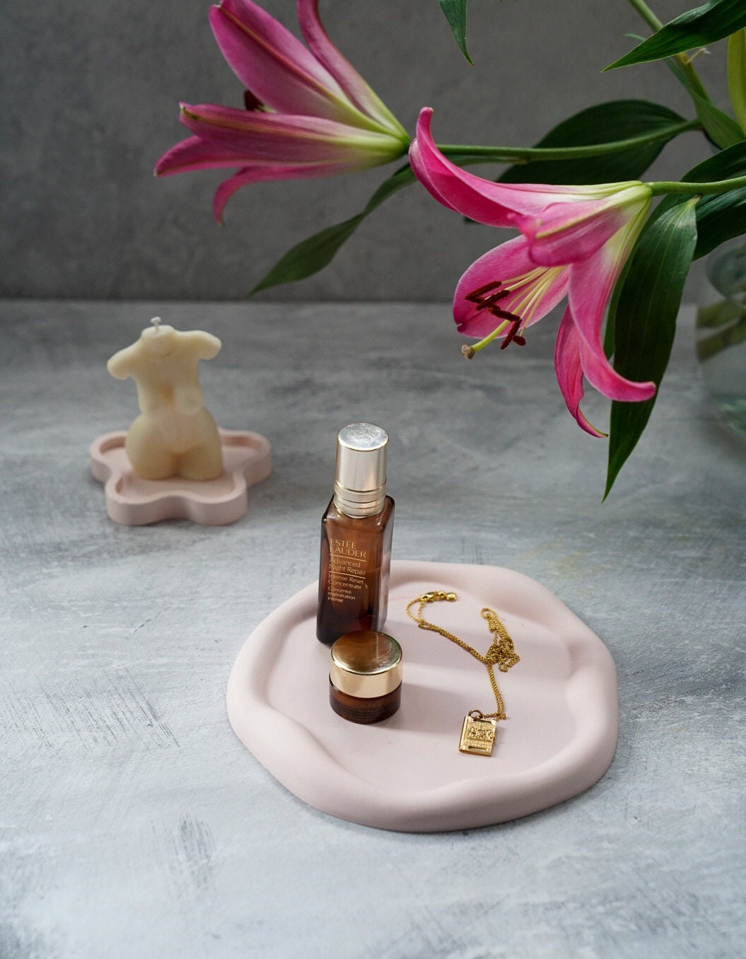 Powder Pink Curvy Round Trinket Tray wIth some facial products  and jewels on it, on the background female body candle with daisy shape coaster. 