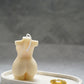 Curvy Goddess Candle from the back on a trinket tray with gold earrings on it. 