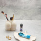 Stoneware bottom vase with some makeup brush in it with a grey background with a trinket tray and cream on it.